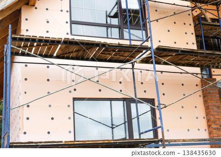 Foam insulation panels on external wall, scaffolding setup, mounting board, facade renovation, energy-efficient cladding, construction, building improvement, adhesive fixing. Foam insulation panels on external wall, scaffolding setup, mounting board, facade renovation, energy-efficient cladding, construction, building improvement, adhesive fixing. 138435630