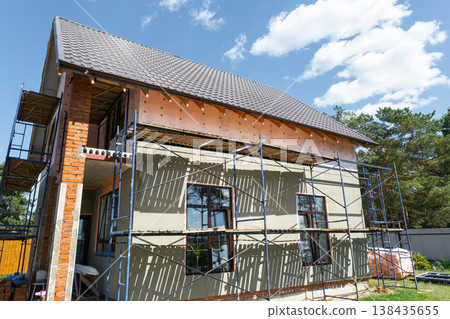 Exterior wall covered by facade plaster, scaffolding structure assembly, finishing stage, mesh layer reinforcement, renovation and leveling, protective surface. Exterior wall covered by facade plaster, scaffolding structure assembly, finishing stage, mesh layer reinforcement, renovation and leveling, protective surface. 138435655
