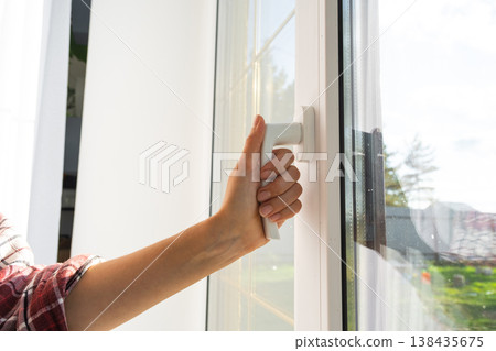 Hand opens PVC window for fresh air ventilation, featuring double-glazed unit, modern fittings, benefits for comfort, draft protection, and sound insulation, installation business solution. 138435675
