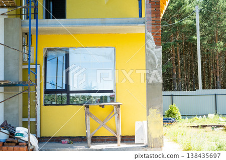 Yellow facade paint on house, over plaster layer, decorative wood elements (if present), final wall finish, external renovation, architectural detail, scaffolding visible. Yellow facade paint on house, over plaster layer, decorative wood elements (if present), final wall finish, external renovation, architectural detail, scaffolding visible. 138435697