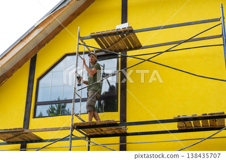 Final yellow painting of house facade, completed plaster finish, timber boards attached (if present), half-timber architectural accent, exterior decorative effect. 138435707
