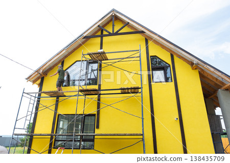 Finished house facade, exterior yellow paint over plaster, decorative timber boards, half-timber framing, wall protection, modern construction, final cladding stage. 138435709
