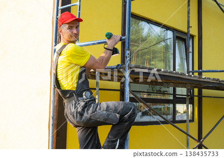 Handyman on scaffolding with drill, facade repair, professional exterior work, renovation, builder tools, on-site specialist for house improvements and painting. Handyman on scaffolding with drill, facade repair, professional exterior work, renovation, builder tools, on-site specialist for house improvements and painting. 138435733
