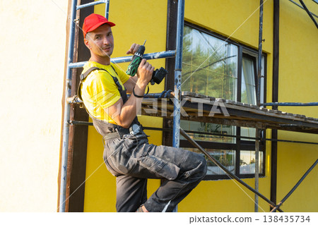 Construction worker sitting on scaffold with power tool, facade restoration, painting and installation, handyman service at home, professional repairs and consultation. Construction worker sitting on scaffold with power tool, facade restoration, painting and installation, handyman service at home, professional repairs and consultation. 138435734