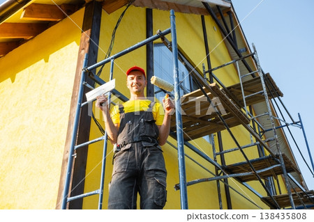 Builder standing with paint roller, facade repair, scaffolding, renovation, tools, handyman home improvement service, consultation, expert in finishing works. Builder standing with paint roller, facade repair, scaffolding, renovation, tools, handyman home improvement service, consultation, expert in finishing works. 138435808