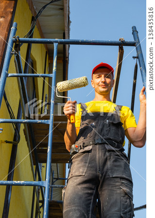 Young construction worker holding roller, scaffolding, facade painting, wall repairs, home improvement, handyman tools, repair business, consulting service visit. 138435816