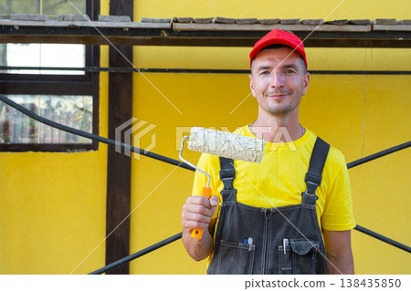 Portrait of builder with paint roller, home painting, at-home repairs, handyman services, private renovation business, DIY equipment kit, wall improvement. Portrait of builder with paint roller, home painting, at-home repairs, handyman services, private renovation business, DIY equipment kit, wall improvement. 138435850