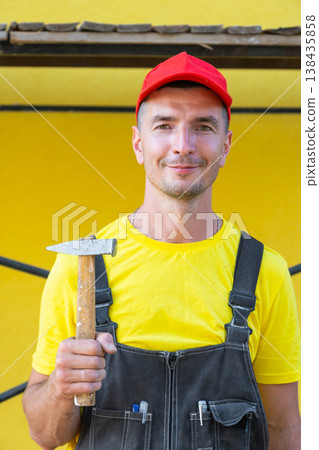 Portrait of construction worker in yellow shirt with hammer, private repair business, nailing, framing, carpentry work, home visit, do-it-yourself skills. Portrait of construction worker in yellow shirt with hammer, private repair business, nailing, framing, carpentry work, home visit, do-it-yourself skills. 138435858