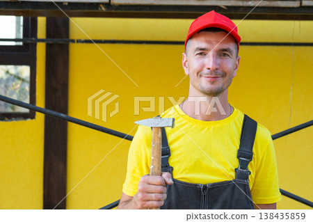 Builder portrait with hammer, ready for house construction, private specialist for home repairs, DIY, framing, nailing, consultation at building site. Builder portrait with hammer, ready for house construction, private specialist for home repairs, DIY, framing, nailing, consultation at building site. 138435859