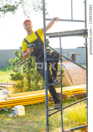 Portrait of construction worker on scaffolding with cordless screwdriver, on-site home renovation, handyman service, private business, building improvement. Portrait of construction worker on scaffolding with cordless screwdriver, on-site home renovation, handyman service, private business, building improvement. 138435862