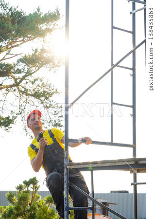 Builder with screwdriver stands on scaffolding, home repairs, private business handyman, on-site assembly, DIY installation, expert consultation, maintenance. Builder with screwdriver stands on scaffolding, home repairs, private business handyman, on-site assembly, DIY installation, expert consultation, maintenance. 138435863