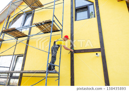 Facade worker fastening wood slats for decorative half-timbered finish, stylish home exterior, craftsman job, cladding elements, renovation services. 138435893