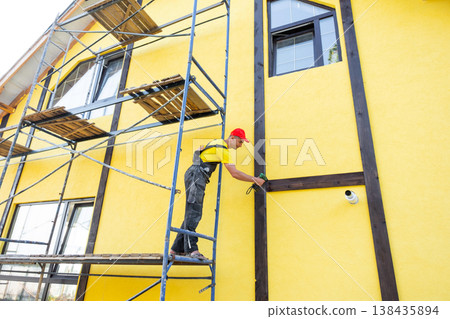 Skilled exterior builder attaches wooden beams in half-timber style, decorative house facade, home improvement, construction, expert renovation work. Skilled exterior builder attaches wooden beams in half-timber style, decorative house facade, home improvement, construction, expert renovation work. 138435894