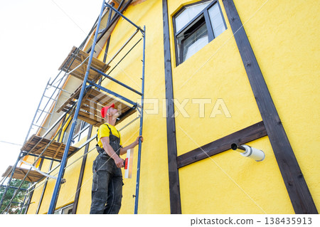 Facade technician with trowel, carrying out plastering and finishing, smooth wall preparation, private business, renovation, craftsman expertise at height. 138435913