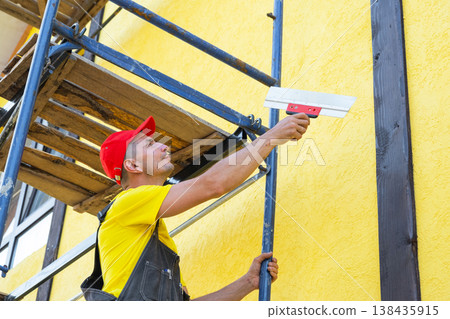 Plaster contractor on facade, using trowel for fine wall finish, leveling, restoration, decorative and preparatory works, private home renovation business. 138435915