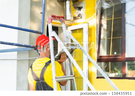 Construction worker portrait with ladder in front of house, home repair project, builder ready for onsite service and maintenance business. Construction worker portrait with ladder in front of house, home repair project, builder ready for onsite service and maintenance business. 138435951