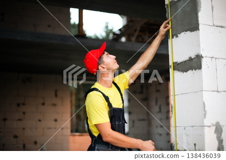 Construction worker checks vertical height of window opening, site measurements for installation, planning wall partitions, building renovation tasks. 138436039