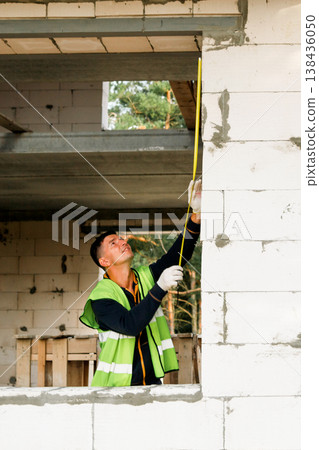 Construction specialist works at window, bricklaying, checks frame fit, alignment tasks, organization, wall build, technical measurement and teamwork, repair action. Construction specialist works at window, bricklaying, checks frame fit, alignment tasks, organization, wall build, technical measurement and teamwork, repair action. 138436050
