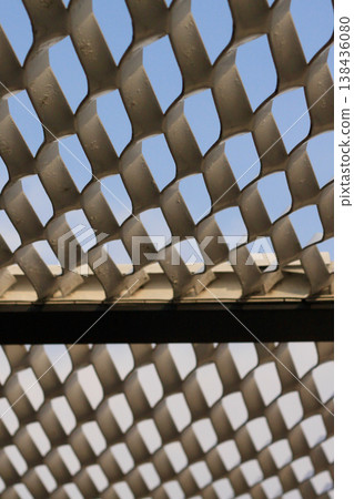 White expanded metal mesh pattern and geometric pattern against a blue sky background. 138436080