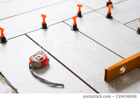 Close-up of tile leveling system during floor tiling, spacers and measurement tape, home repair work, precise ceramic flooring installation. 138436098