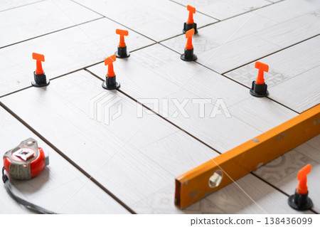 Floor tiling in progress, ceramic tiles with spacers and leveling system, repair and renovation work, home improvement, professional installation tools. 138436099