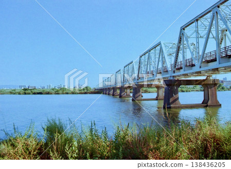 一座桁架橋在藍天下延伸，河岸景色優美。 138436205