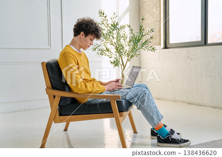 Portrait handsome young male typing on laptop sitting on chair at home Portrait handsome young male typing on laptop sitting on chair at home 138436620