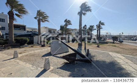 A square with a large anchor object surrounded by palm trees near the coast under a blue sky on a windy day A square with a large anchor object surrounded by palm trees near the coast under a blue sky on a windy day 138436770