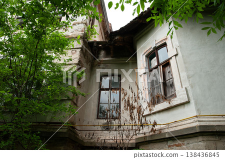 Weathered Historic Building Facade Overgrown With Green Trees And Dead Vines Showing Peeling Paint And Old Windows In Natural Light Weathered Historic Building Facade Overgrown With Green Trees And Dead Vines Showing Peeling Paint And Old Windows In Natural Light 138436845