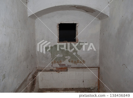 Dilapidated Room Interior With Peeling White Walls, Exposed Brickwork, Small Dark Window And Vintage Floral Wallpaper Remnants In An Abandoned Building Setting Dilapidated Room Interior With Peeling White Walls, Exposed Brickwork, Small Dark Window And Vintage Floral Wallpaper Remnants In An Abandoned Building Setting 138436849