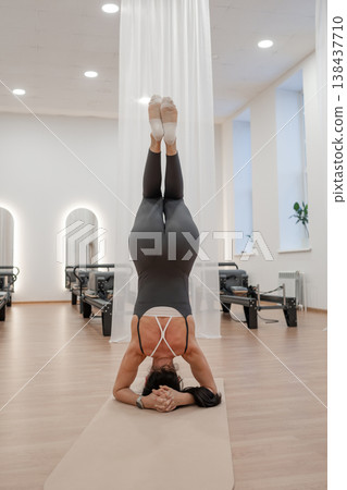 Flexible woman doing advanced headstand balance yoga pose on mat in bright serene studio. Advanced headstand, yoga pose, mat, balance, bright studio. Flexible woman doing advanced headstand balance yoga pose on mat in bright serene studio. Advanced headstand, yoga pose, mat, balance, bright studio. 138437710