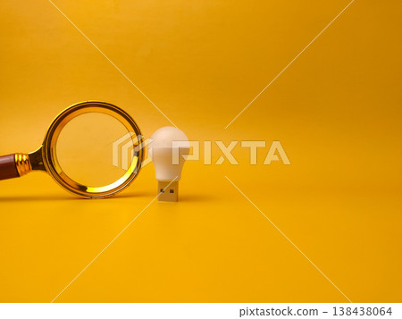 A minimalist studio shot featuring a golden magnifying glass placed next to a small white USB LED light bulb. 138438064