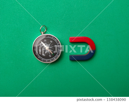 A high-angle conceptual flat lay on a vibrant green background featuring a magnetic compass and horseshoe magnet. A high-angle conceptual flat lay on a vibrant green background featuring a magnetic compass and horseshoe magnet. 138438090