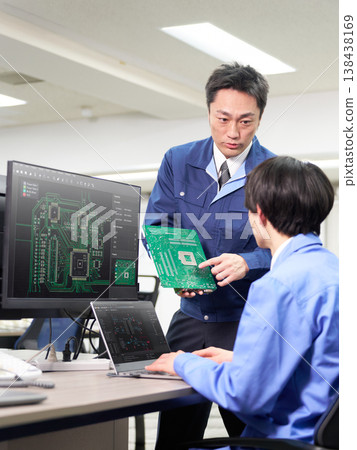 A manufacturing engineer programming while checking the printed circuit board and wiring diagram. A manufacturing engineer programming while checking the printed circuit board and wiring diagram. 138438169