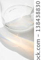 Minimalist detail of a glass bottle and a water ripple, showing a bright, soft rainbow caustics light refractions on white textured paper 138438830