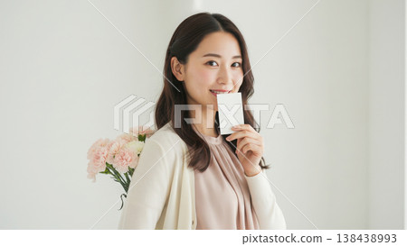 一位女士面帶微笑,背上藏著一朵康乃馨,手裡拿著一張「謝謝」卡片。 一位女士面帶微笑,背上藏著一朵康乃馨,手裡拿著一張「謝謝」卡片。 138438993