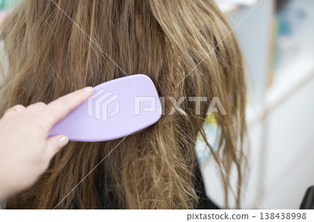 Hand combing tangled brown hair with a purple brush 138438998