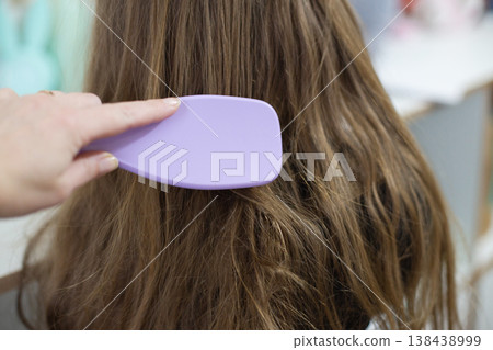Hand combing tangled brown hair with a purple brush Hand combing tangled brown hair with a purple brush 138438999