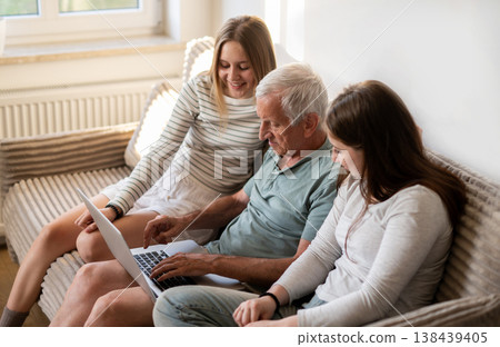 Happy Sisters And Granddad Surfing The Internet Together On The Sofa In A Cozy Room Happy Sisters And Granddad Surfing The Internet Together On The Sofa In A Cozy Room 138439405
