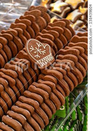 Captured from a macro perspective, a mitten-shaped gingerbread cookie with an intricate white royal icing snowflake design stands out against a background of stacked cookies. The detailed decoration 138439604