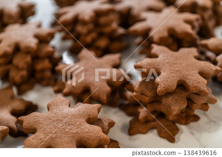 Side view of chocolate ginger snowflake cookies piled together on a parchment-lined surface, showcasing their festive design and holiday charm. Side view of chocolate ginger snowflake cookies piled together on a parchment-lined surface, showcasing their festive design and holiday charm. 138439616