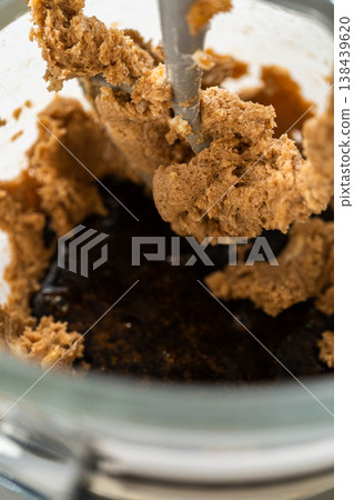 The thick, creamed mixture of butter and sugar is in the mixing bowl. The mixer paddle is beginning to fold the ingredients together, creating a cohesive blend. 138439620