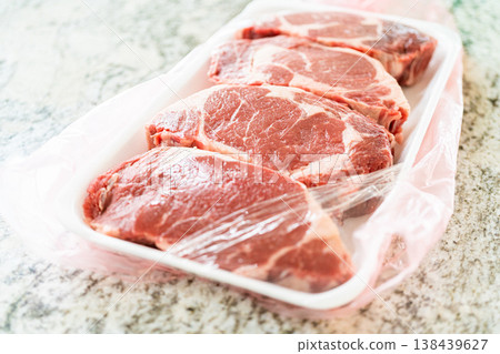 In a sleek, modern white kitchen, a high-quality rib eye steak is carefully being removed from its store packaging. The beautifully marbled steak, soon to be seasoned, promises an upcoming culinary In a sleek, modern white kitchen, a high-quality rib eye steak is carefully being removed from its store packaging. The beautifully marbled steak, soon to be seasoned, promises an upcoming culinary 138439627