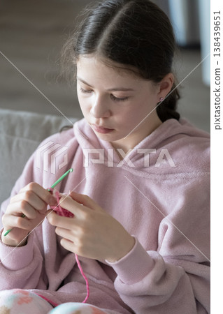 The image shows a teenage girl knitting yarn while sitting indoors. Soft light and relaxed posture create a calm and cozy lifestyle moment. The image shows a teenage girl knitting yarn while sitting indoors. Soft light and relaxed posture create a calm and cozy lifestyle moment. 138439651