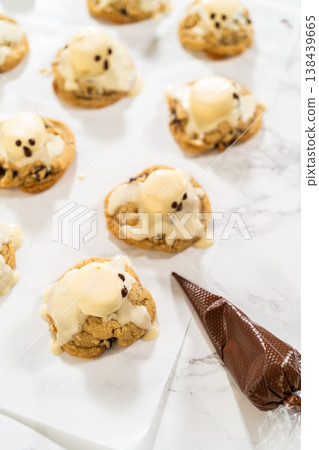 Overhead view of iced cookies arranged on parchment paper with a piping bag nearby. The bright background and soft lighting create a clean cookie decorating layout. 138439665