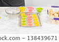 A baking tray filled with colorful flower-shaped cookies coated in yellow, pink, and green sugar, part of the Easter Cookie Sandwich with Raspberry Buttercream recipe. 138439671