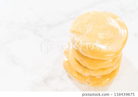 Close-up view of Classic Sugar Cookie Dough wrapped in plastic wrap, prepared for chilling in the refrigerator. This step ensures the dough firms up, making it easier to roll and cut for baking. Close-up view of Classic Sugar Cookie Dough wrapped in plastic wrap, prepared for chilling in the refrigerator. This step ensures the dough firms up, making it easier to roll and cut for baking. 138439675