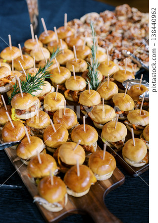 Sizzling Mini Burger Bites Featuring Melted Cheese And Aromatic Rosemary Skewers Displayed At Social Gathering 138440962