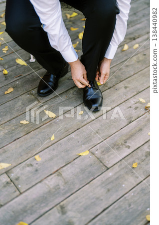 Man Securing Shoe On Wooden Surface During Morning Routine Man Securing Shoe On Wooden Surface During Morning Routine 138440982
