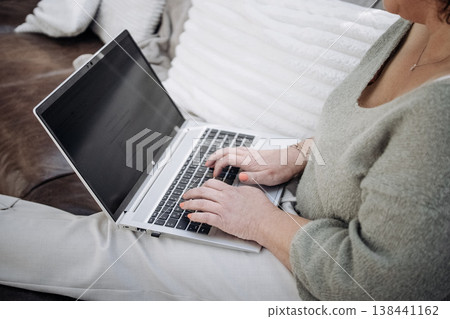 Person Typing On Laptop While Sitting On Sofa: Relaxed Remote Work And Online Browsing In Cozy Living Room At Home Person Typing On Laptop While Sitting On Sofa: Relaxed Remote Work And Online Browsing In Cozy Living Room At Home 138441162